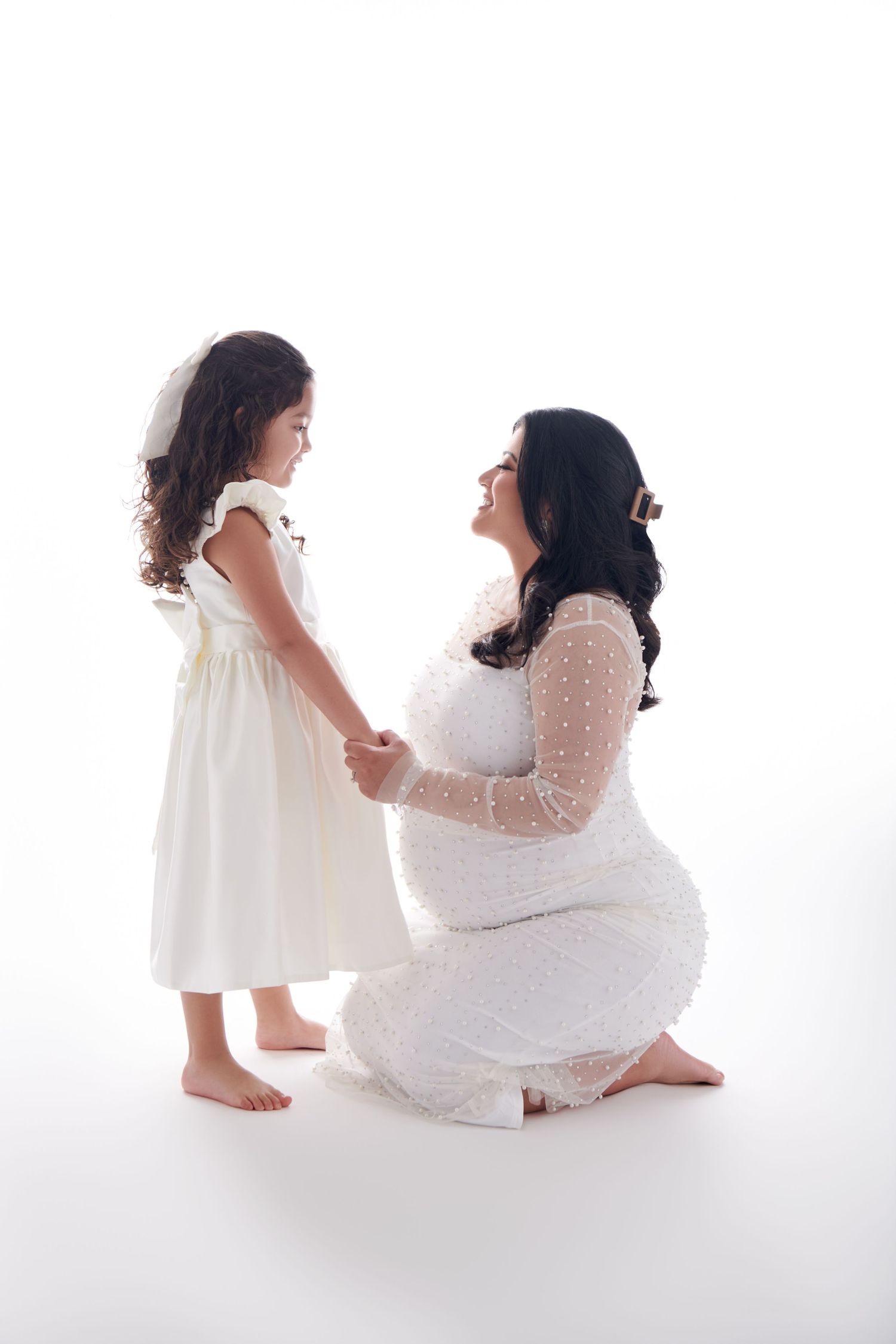 Sweet maternity portrait showing touching moment in white dresses against light backdrop. NJ Studio Maternity Photographer