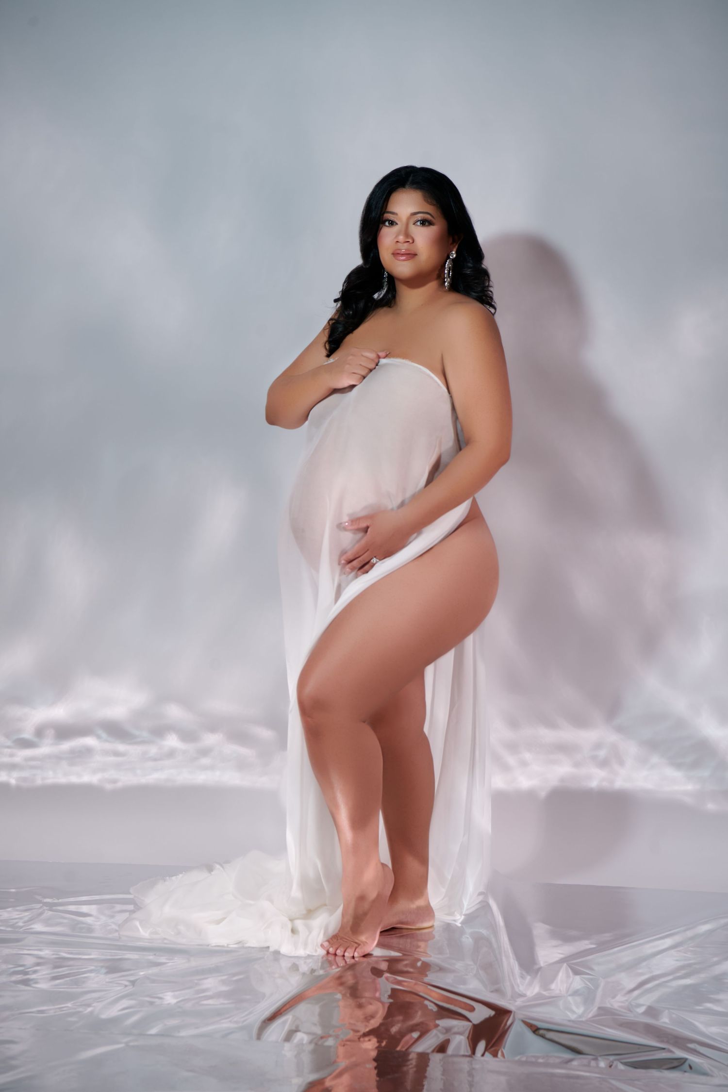 Artistic maternity photoshoot with white sheer fabric and reflective floor in dramatic lighting. NJ Studio Creative Maternity Photographer