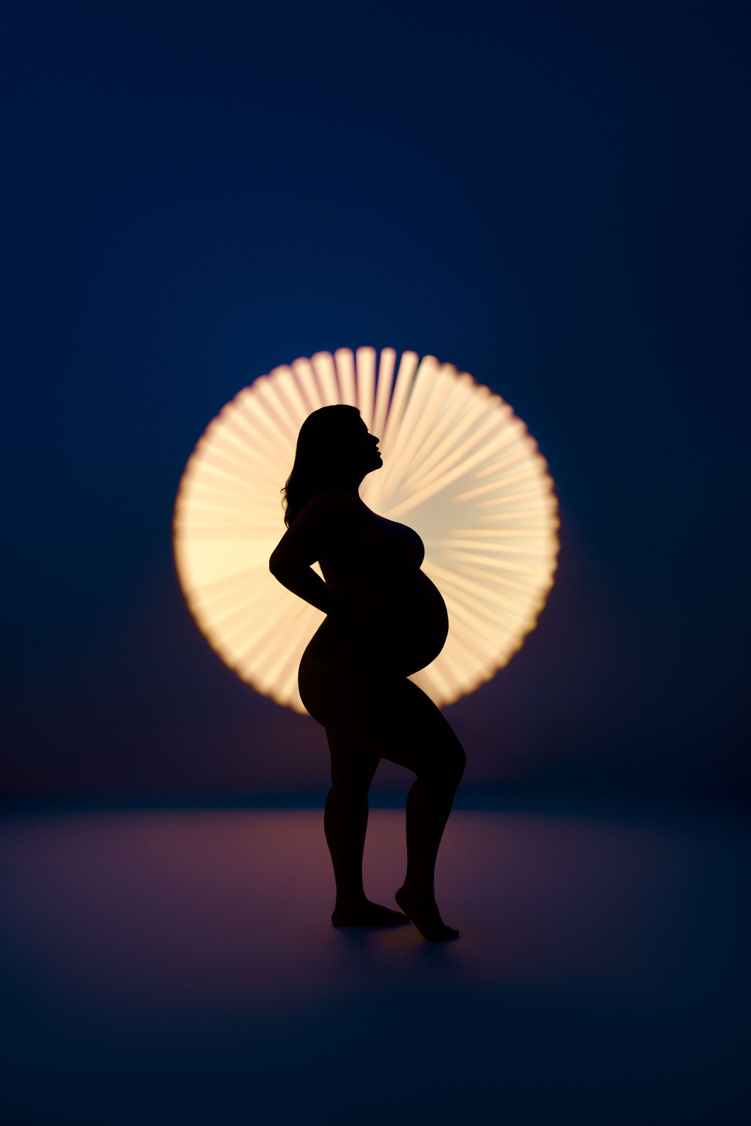 Series of silhouettes against a glowing orange fan or paper umbrella creating a dramatic backlighting effect at sunset. NJ Nutley Maternity