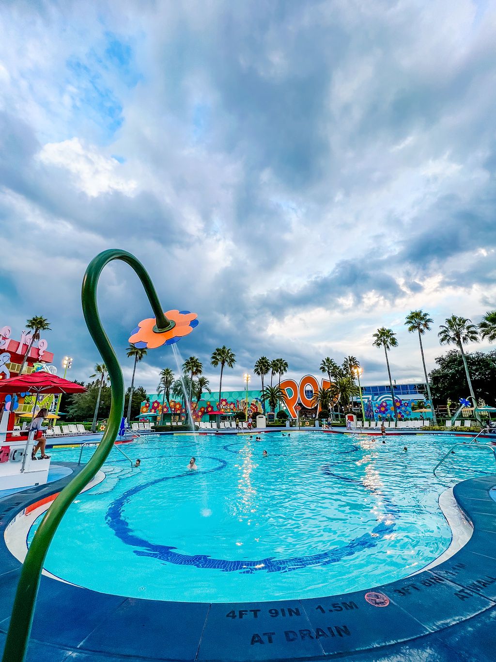 Vibrant pool area with curved design, palm trees, and whimsical decorative elements at Disney resort.