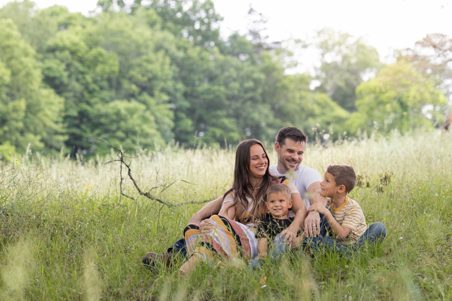 A happy family enjoys a playful moment together in a sunny green summer meadow.
