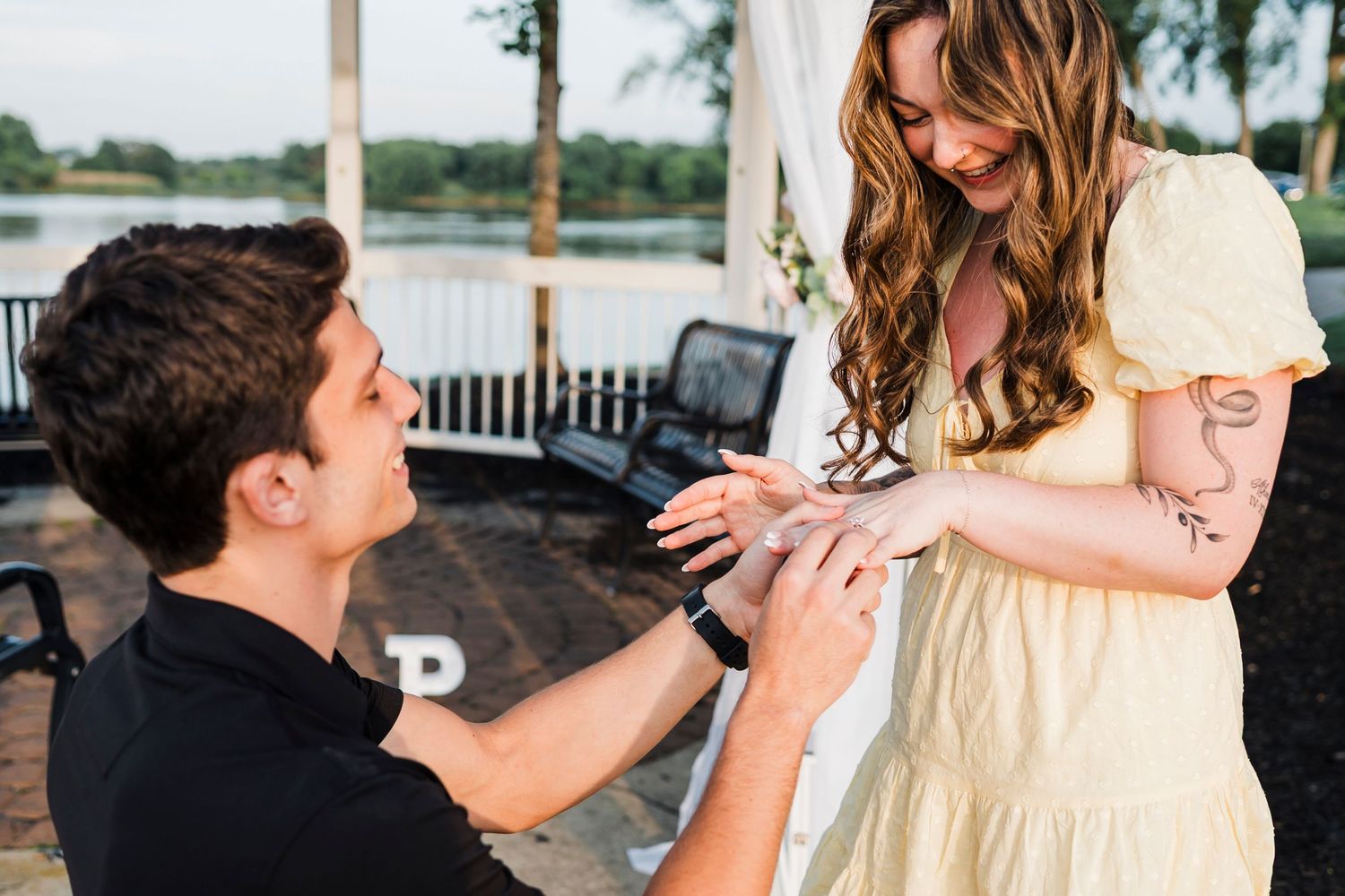 A romantic proposal moment on a waterfront deck, with the proposer kneeling and offering a ring in a warm outdoor setting.