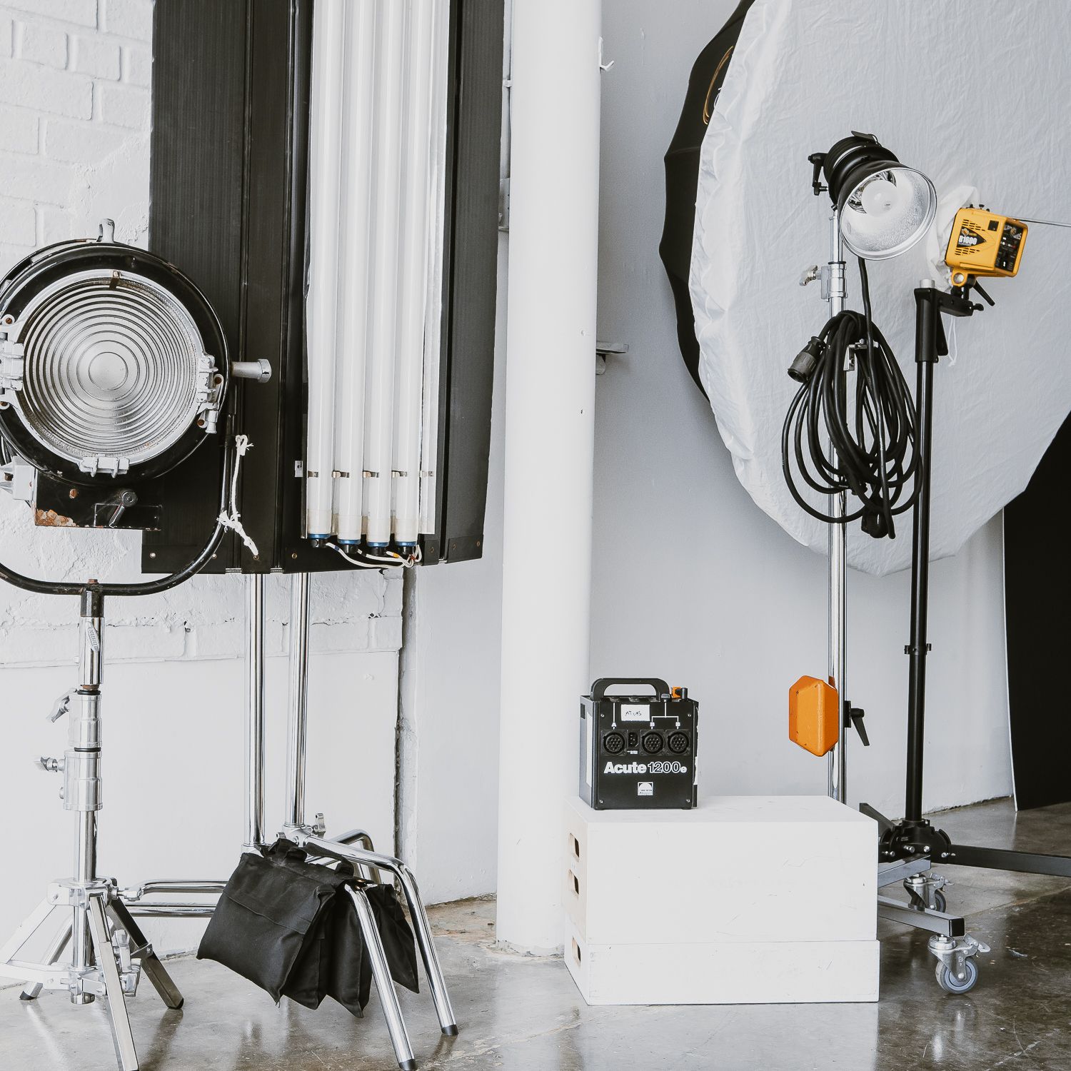 Professional photography studio setup with multiple lights, softboxes and modifiers against white brick wall.