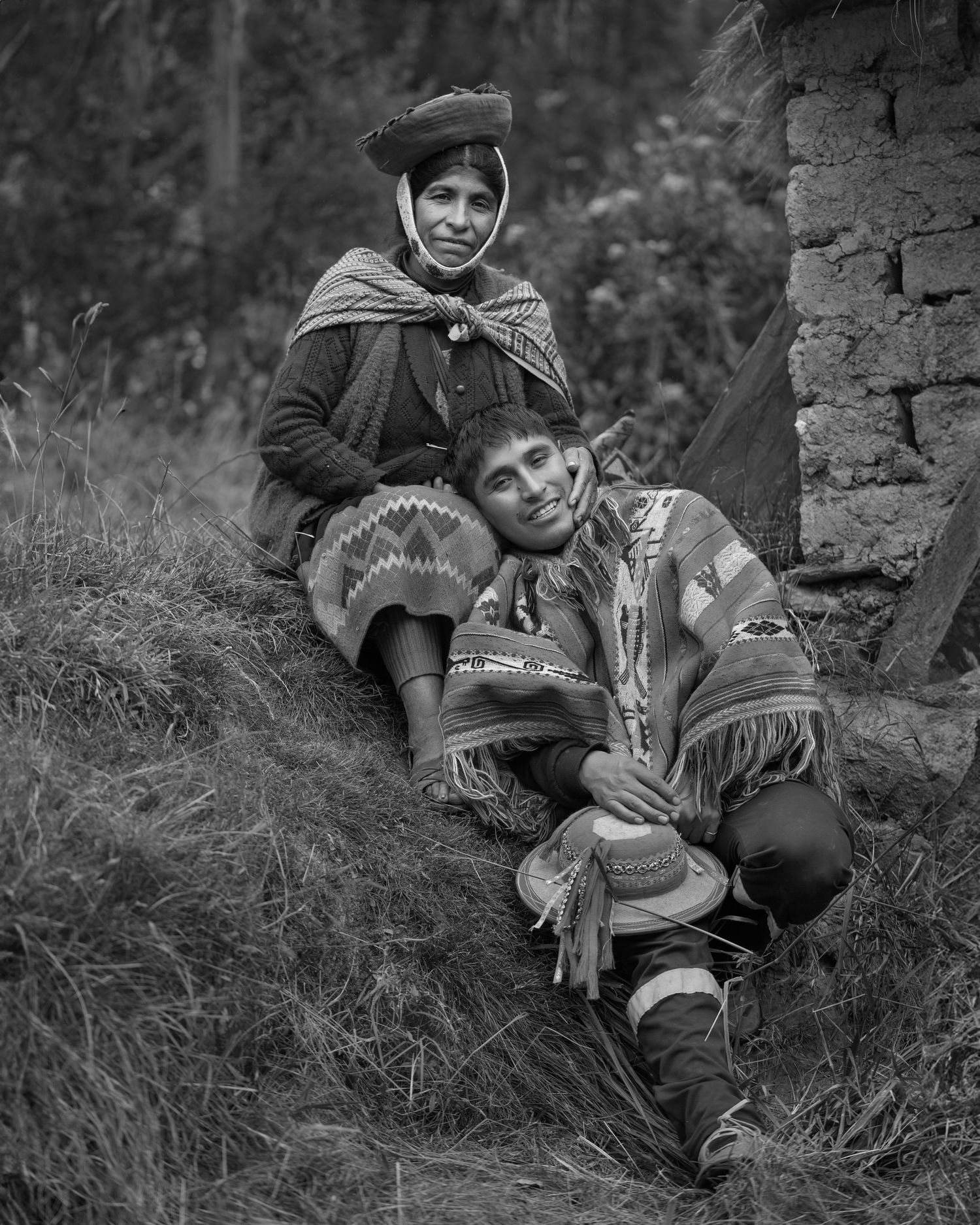 Black and white photo showing traditional Andean dress and textile patterns near stone wall.