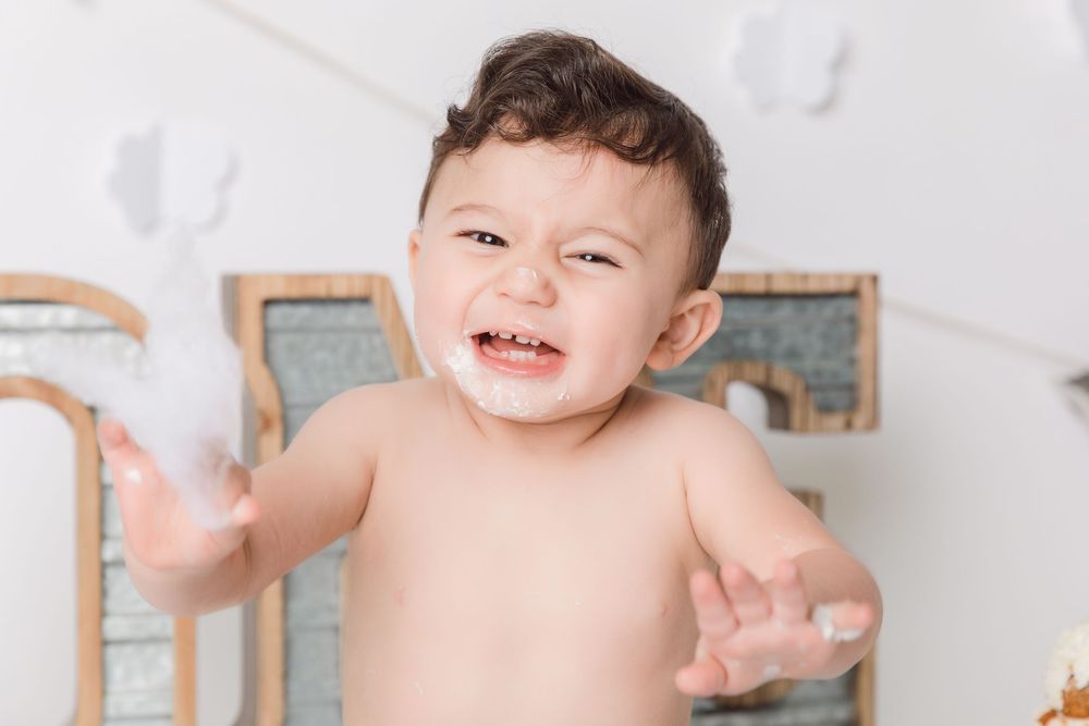 A joyful small figure plays and laughs against a light wood and gray backdrop in a photography studio setting.