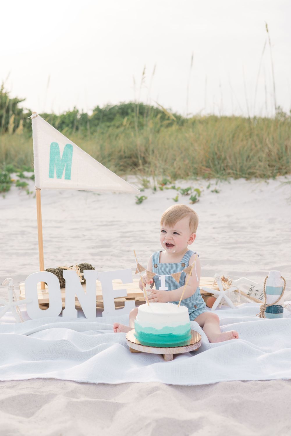 A series of connected photos show a baby enjoying a beach cake smash session surrounded by treats and decorations.