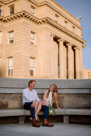 Couple sitting on stone steps outside historic neoclassical building with columns at sunset.