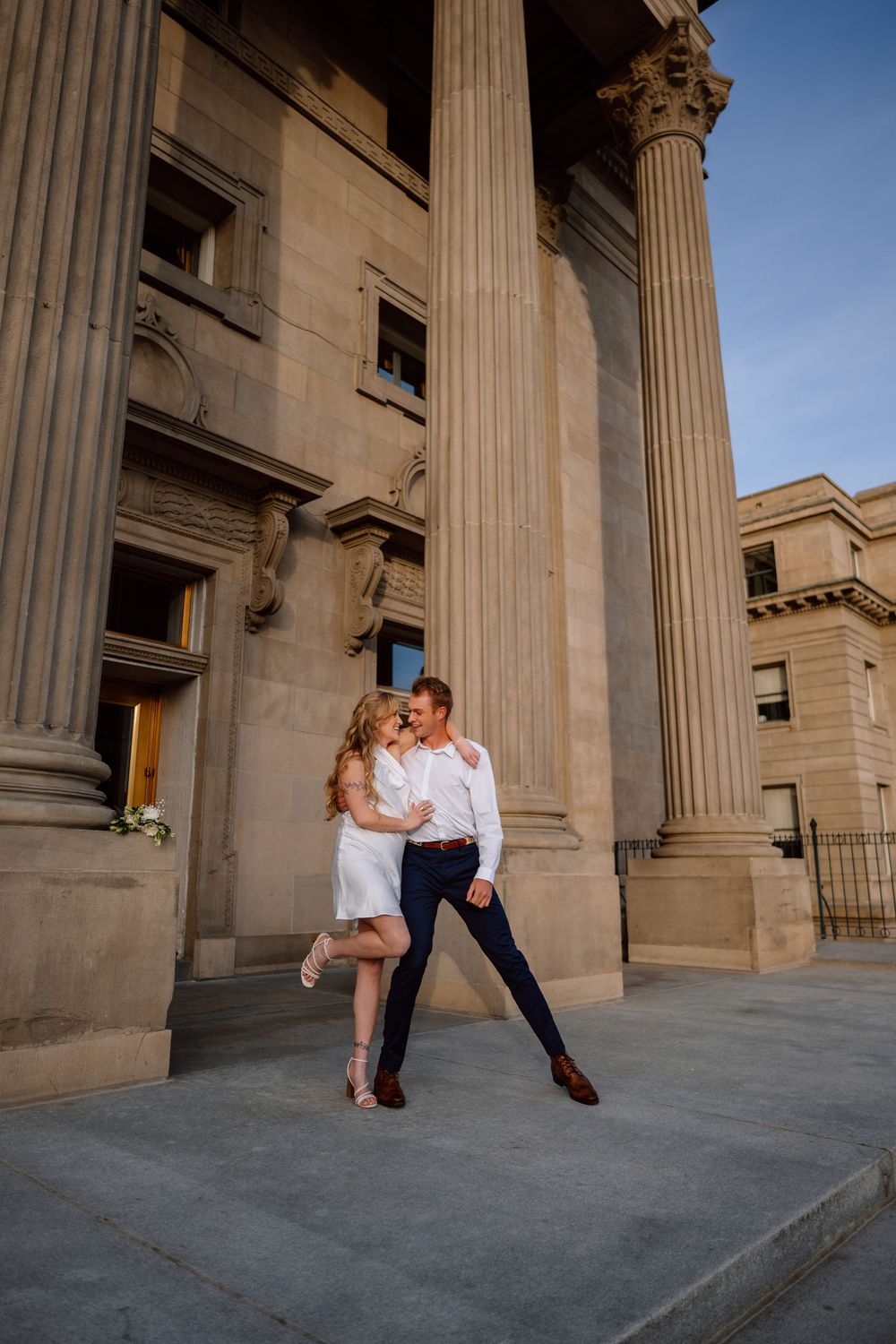 Romantic couple dancing and dipping in elegant poses outside a neoclassical building with stone columns.