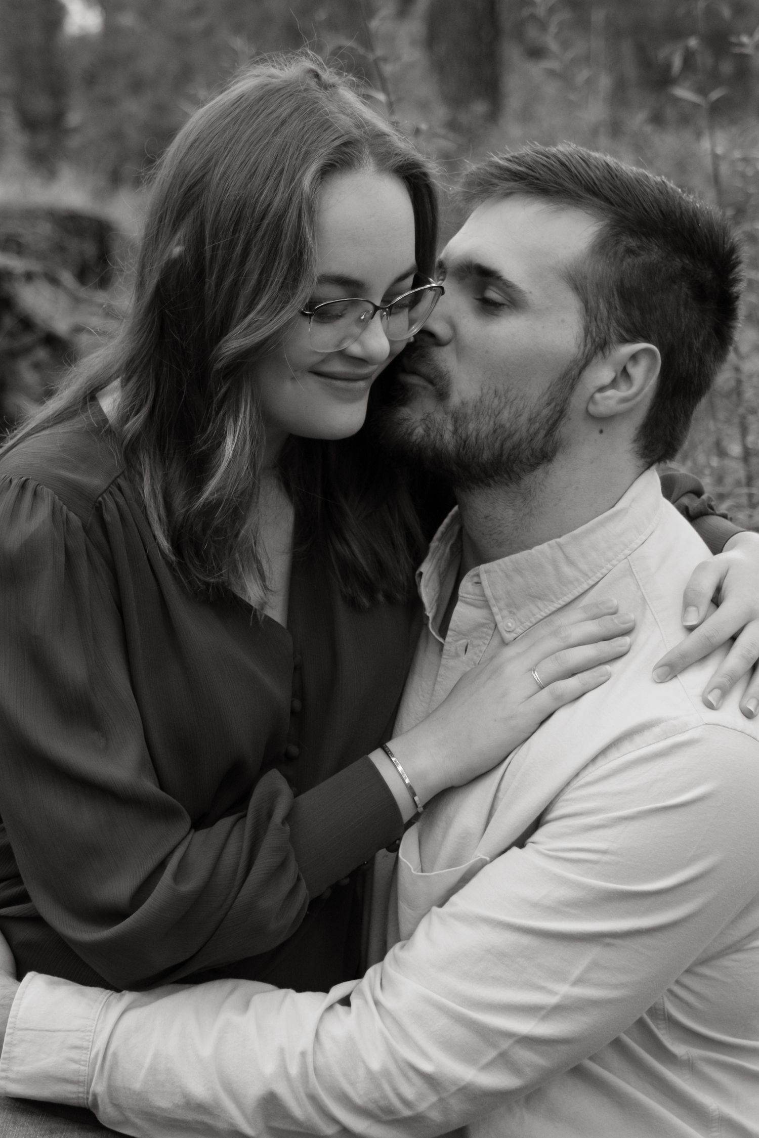 A romantic couple in monochrome tones share tender embraces and laughter while sitting together outdoors in nature.