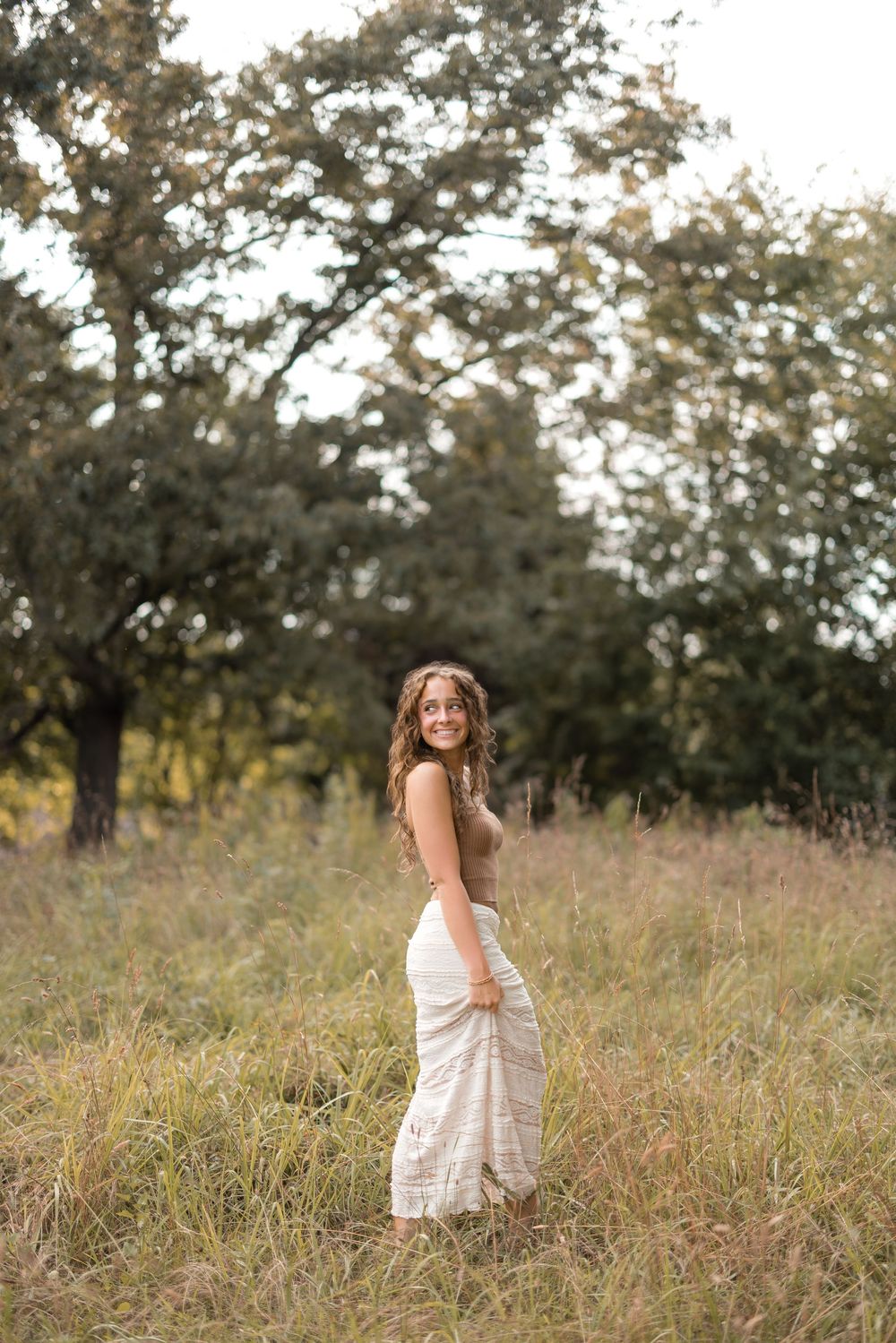 Woman enjoying a sunny afternoon in a grassy meadow while wearing a flowing white dress.