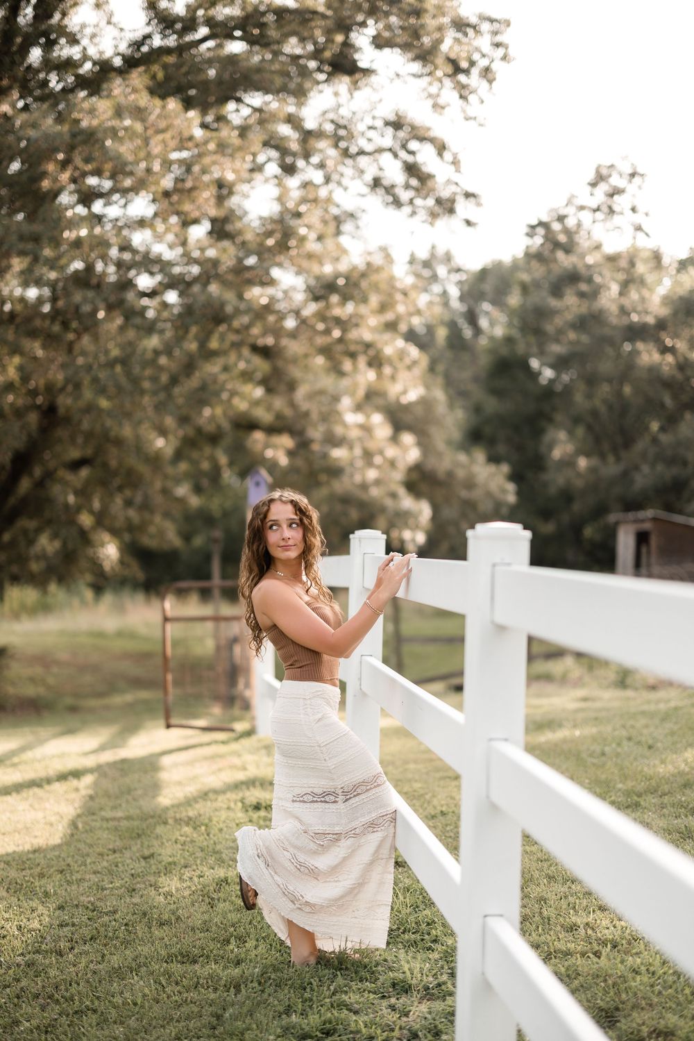 Artistic portrait session with white fence and dreamy lighting in pastoral countryside setting.