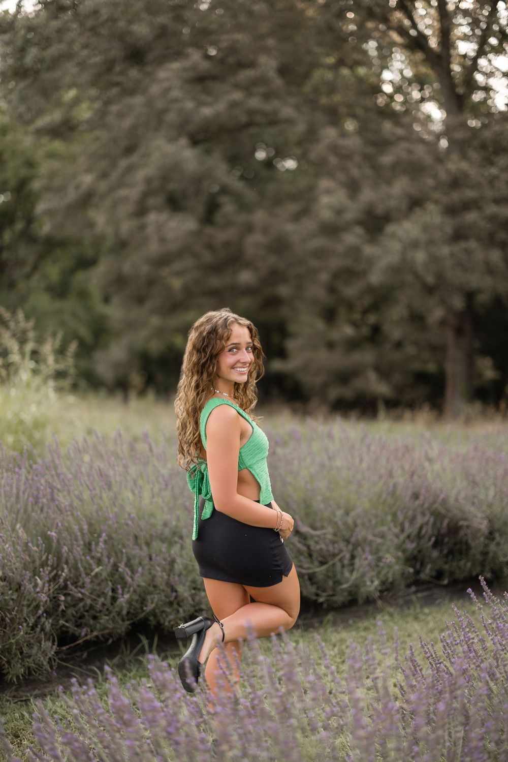 A person poses in a lavender field wearing a green tank top and black shorts on a summer evening.