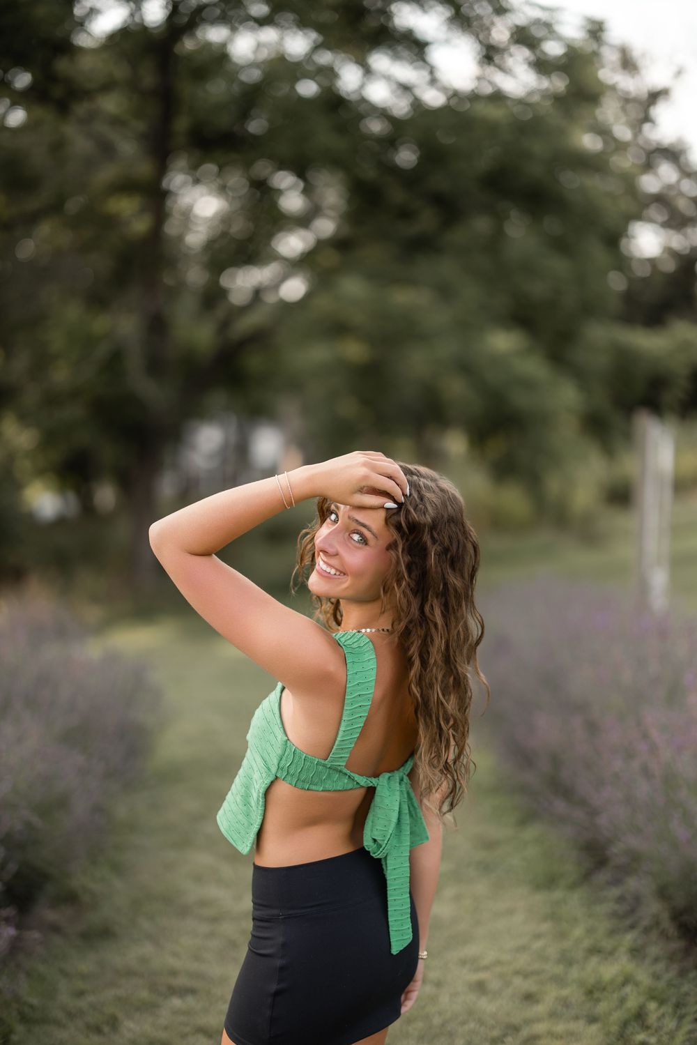 Woman in mint green top and black leggings laughs joyfully while looking upward in a garden setting.