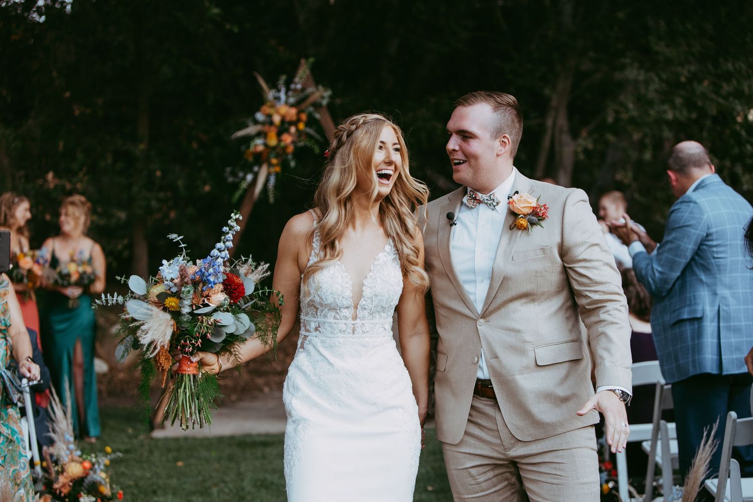 Outdoor wedding ceremony in wooded setting with natural decor and guests.