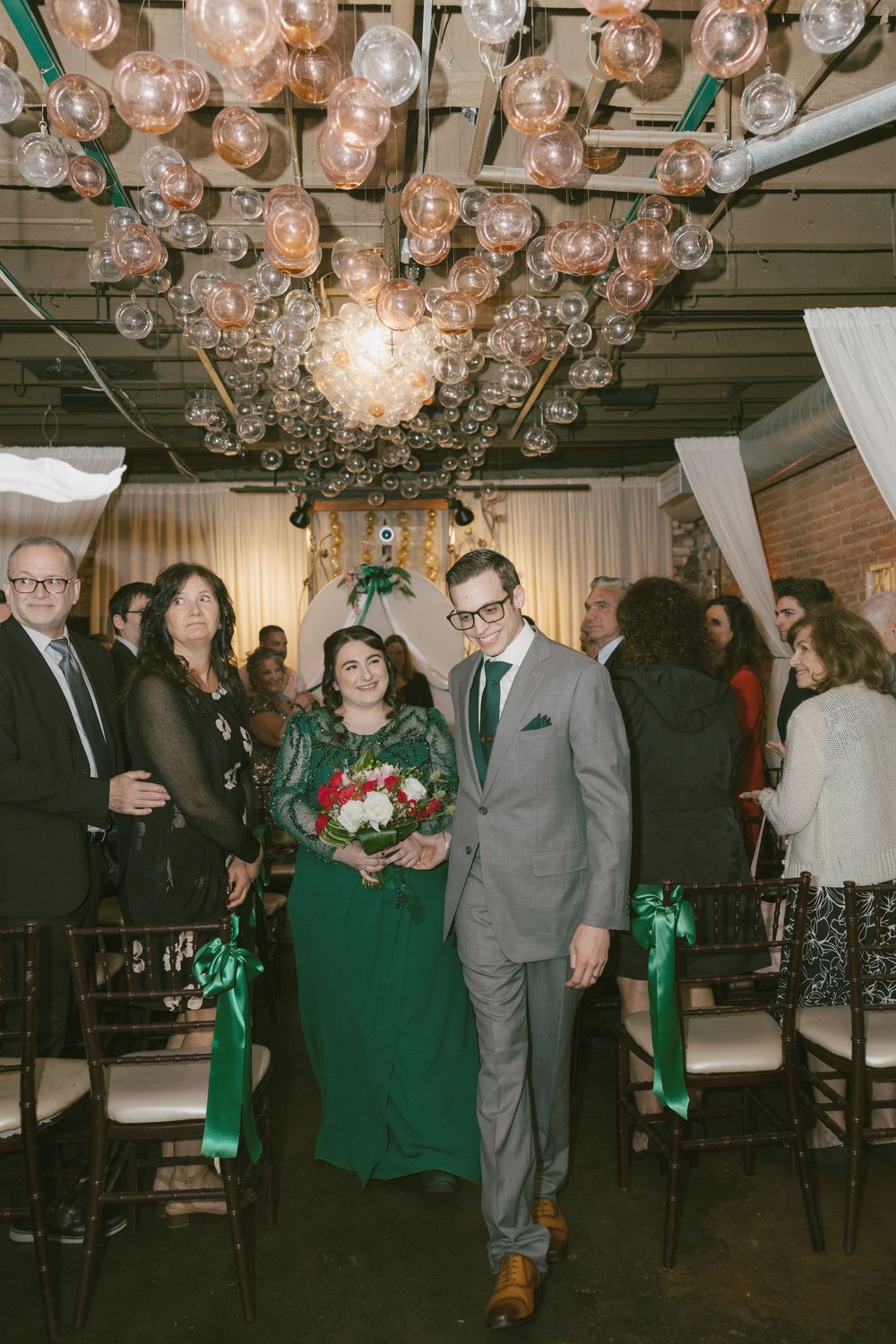 Guests mingling and celebrating at an indoor event with elegant glass bubble lighting and green decor.