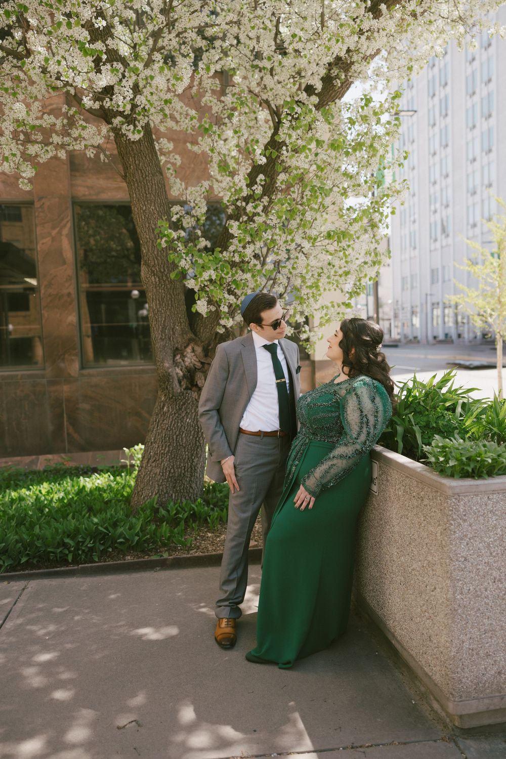 A romantic candid moment beneath a blooming cherry tree in an urban setting.