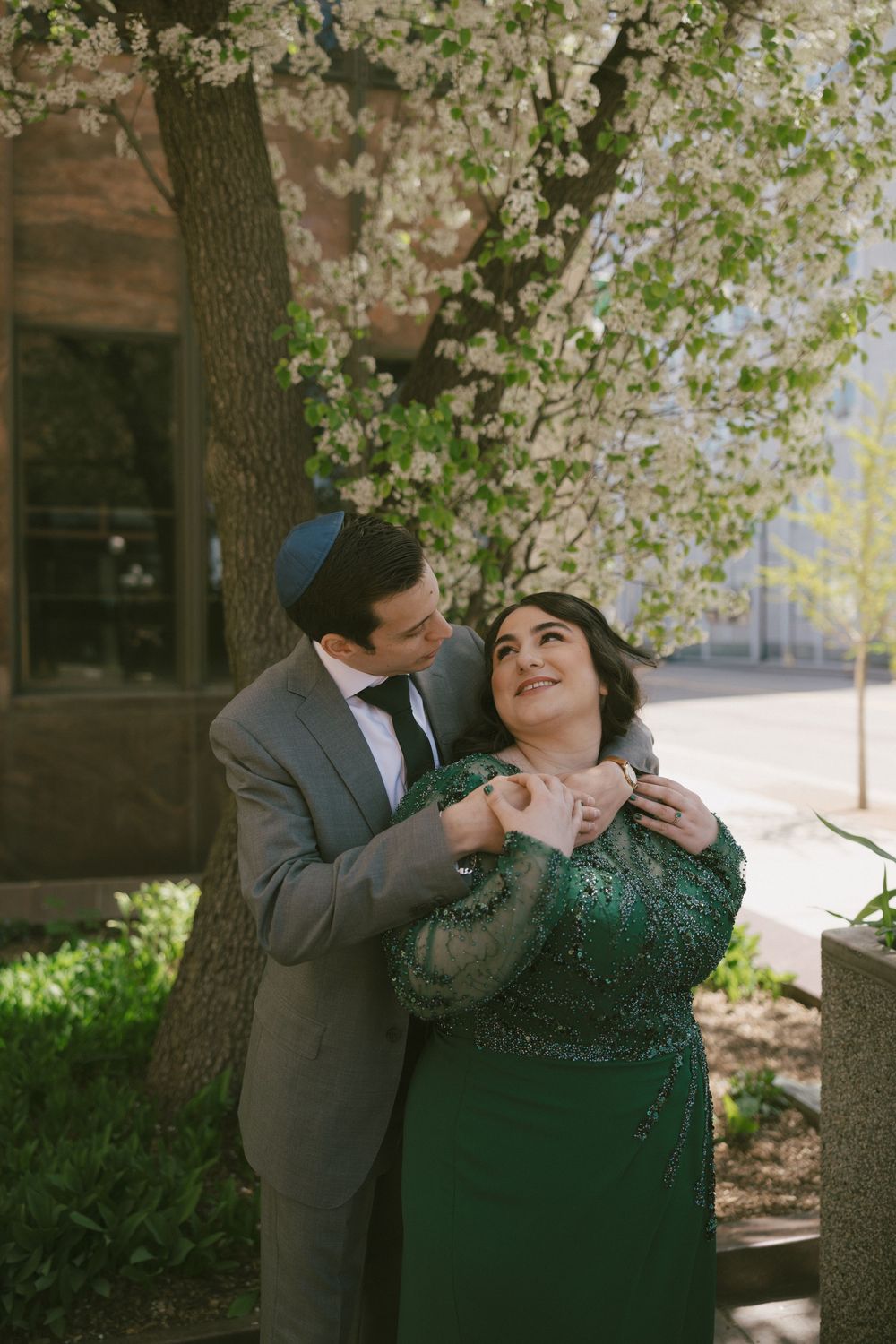 A tender moment between two people in formal attire beneath blooming cherry blossoms.