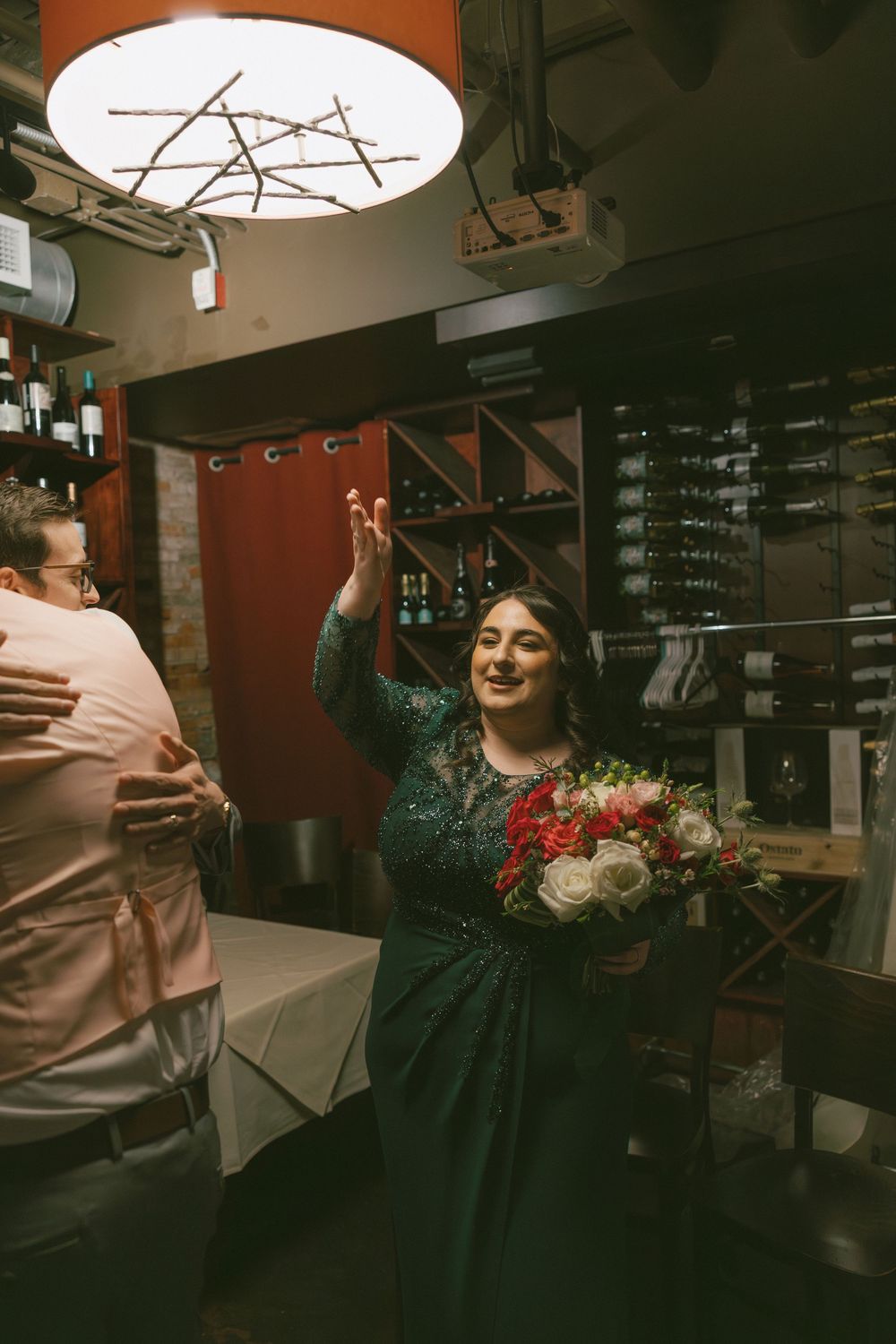 A joyful celebration scene in a dimly lit bar with bouquet of red and white flowers.