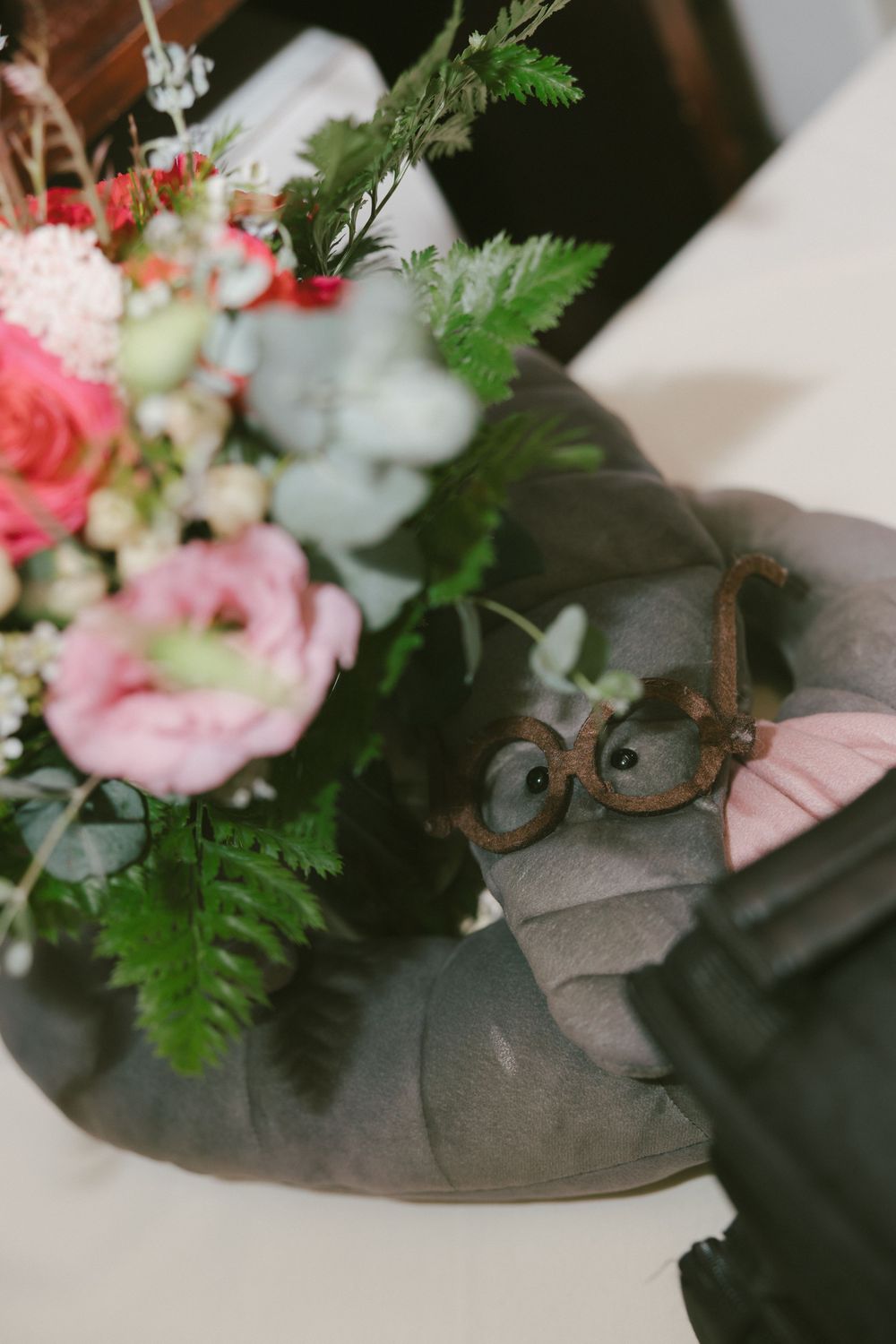 Pink and white floral arrangement with ferns next to decorative glasses on a table.