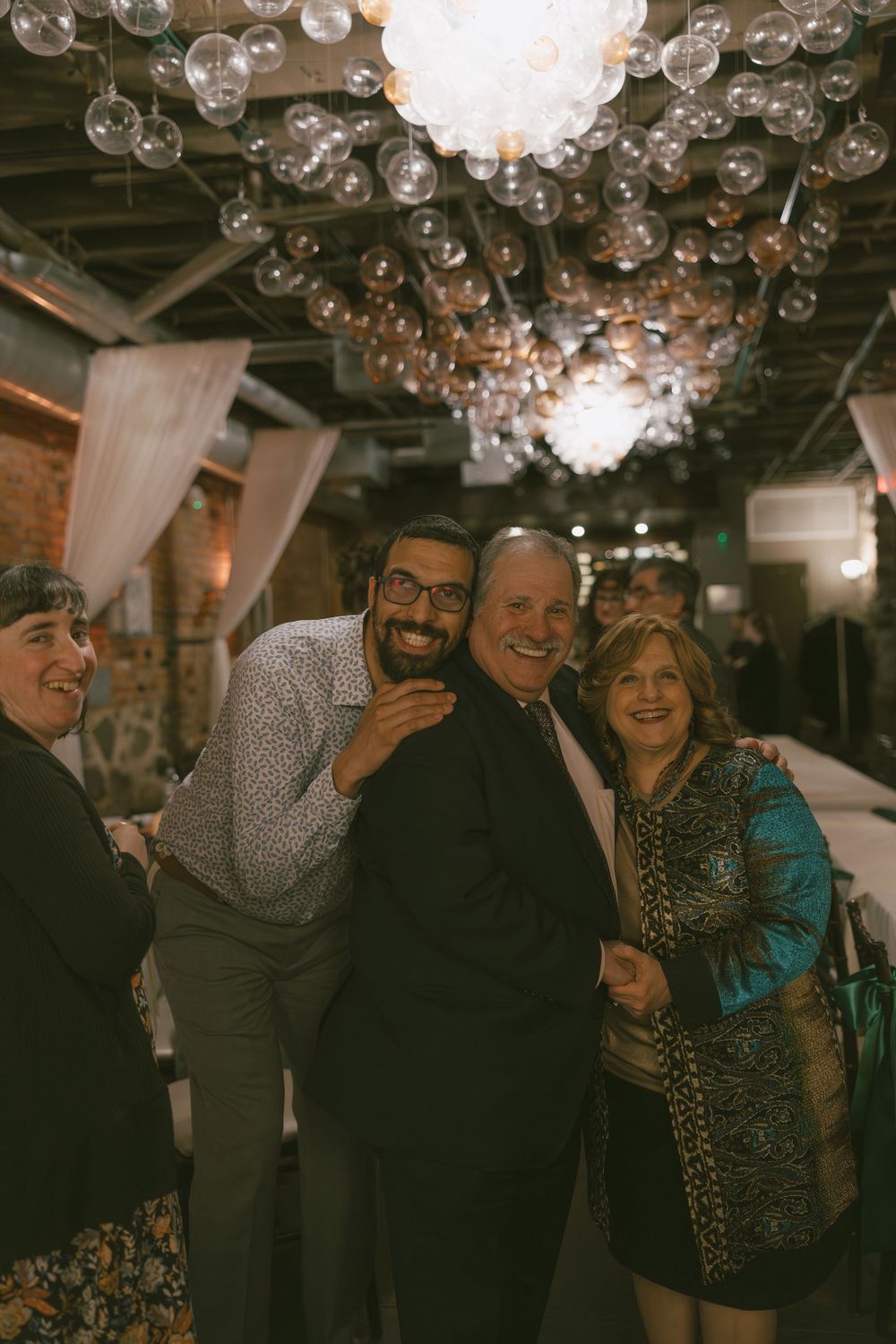 Friends sharing laughter and joy at a celebration under glass bubble chandeliers.