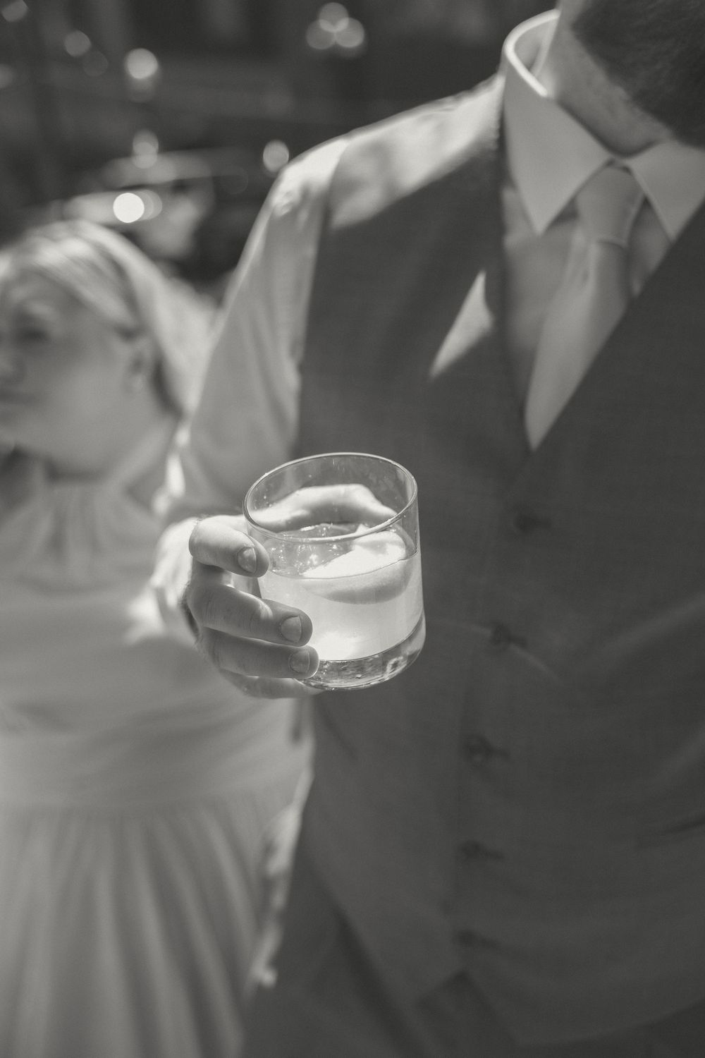 Crystal cocktail glasses being held during a formal event in black and white photography.