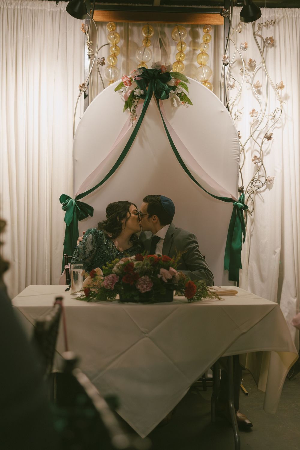 A romantic moment under an elegantly decorated wedding arch with white draping and greenery.