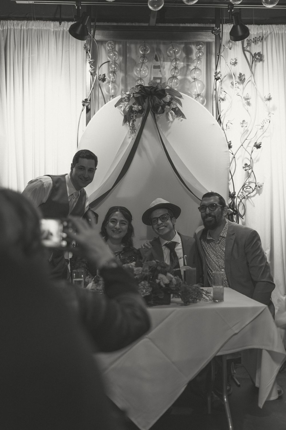 Group of guests enjoying themselves at an indoor reception with white drape backdrop and decorative lighting.