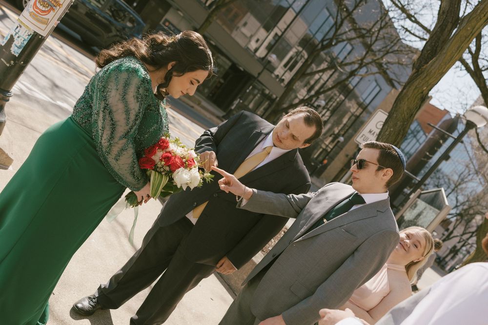 Wedding party members walk down a pathway in a garden setting wearing formal attire and holding bouquets.