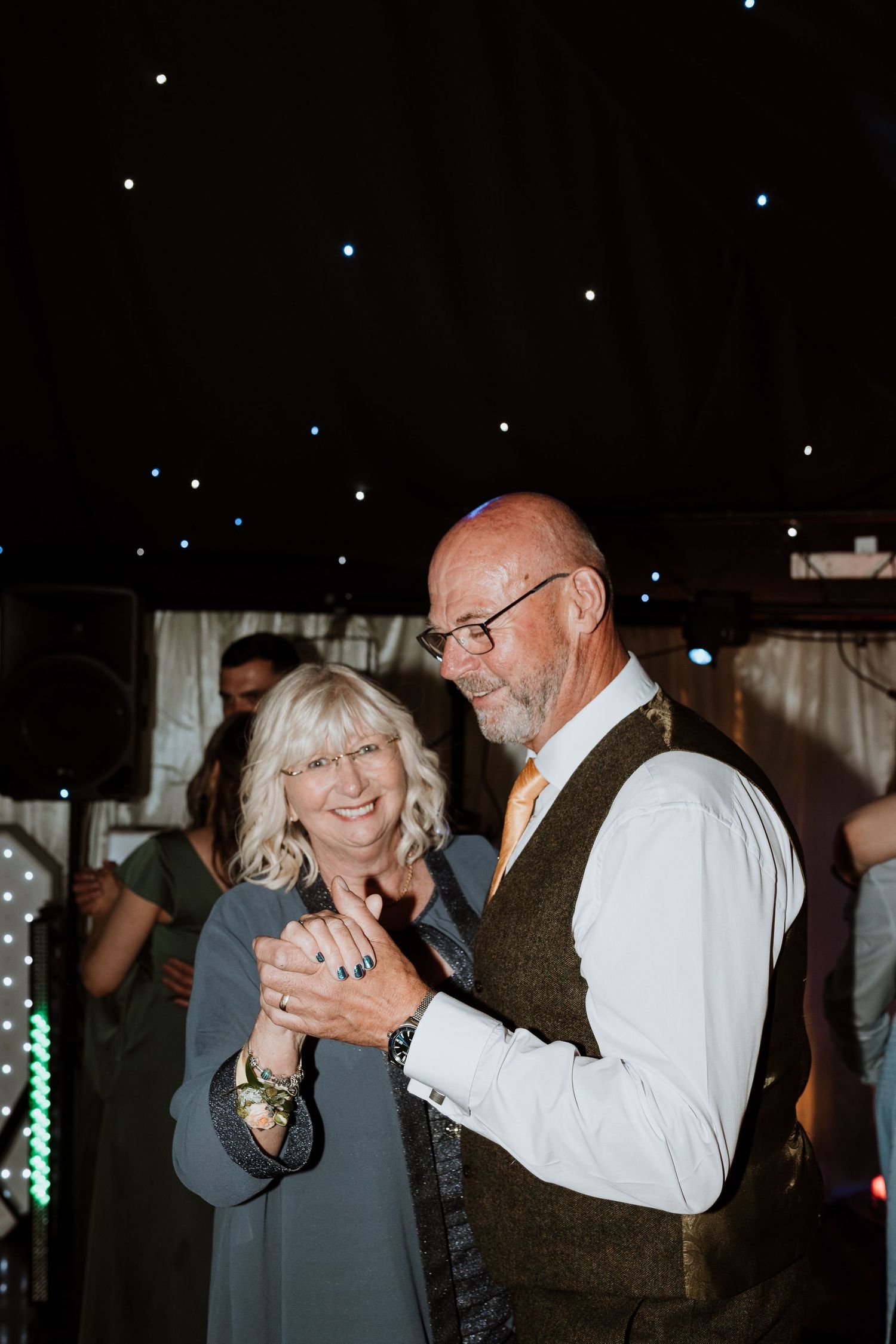A couple dances together under sparkling lights at an evening celebration.