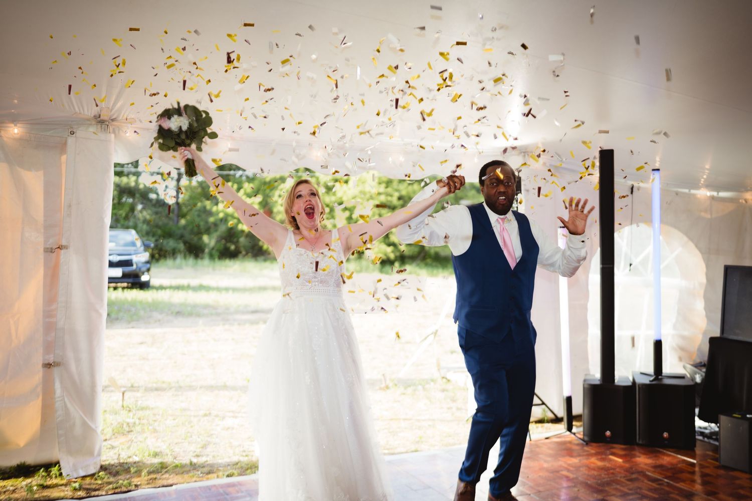 Wedding celebration with confetti falling and guests dancing joyfully under white decor in an elegant venue.