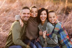 A happy family of four smiles together while sitting outdoors in a field during golden hour.