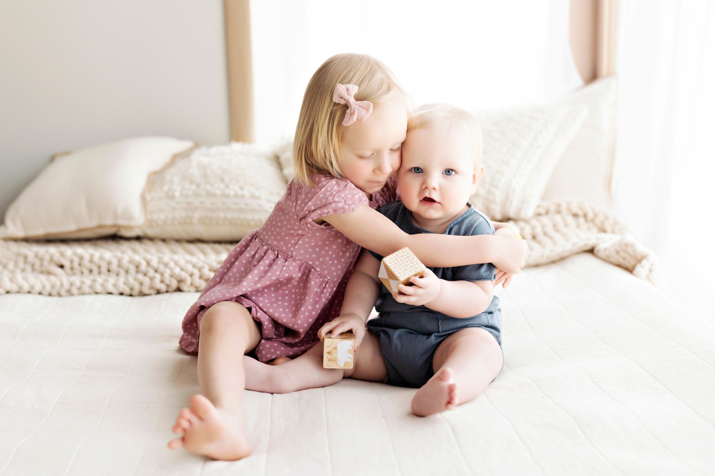 Two young children in casual attire sharing a tender moment on white bedding.