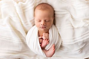 Newborn baby peacefully sleeping wrapped in white fabric.