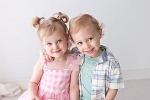 Two toddlers wearing pastel outfits pose together against white background.