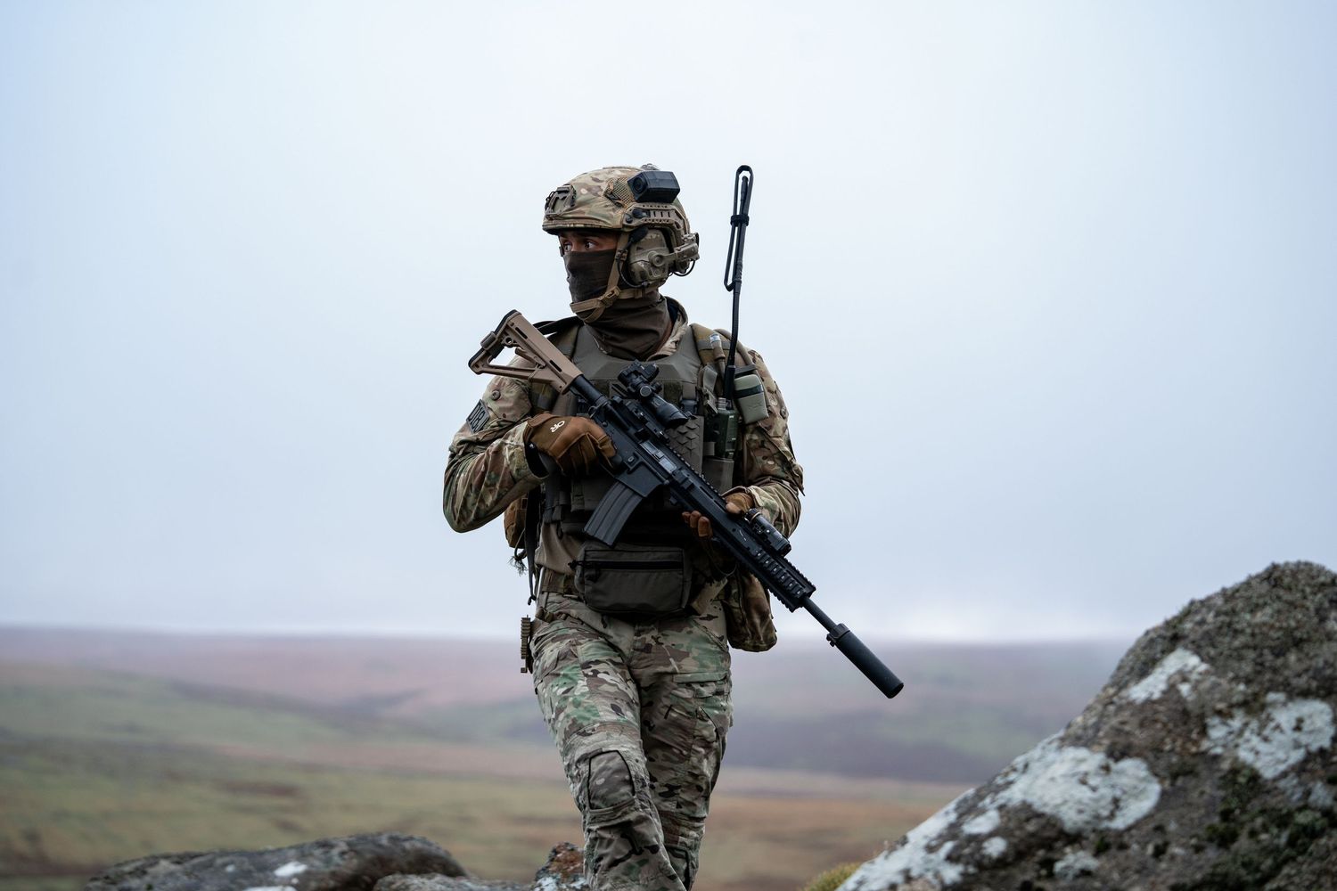 Military personnel in tactical gear patrolling rocky mountainous terrain.