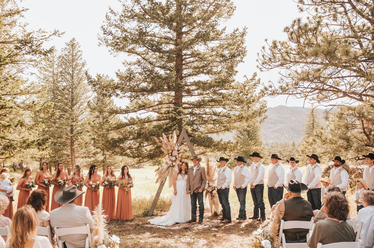 Bride and groom standing in front of a romantic archway, holding hands surrounded by their wedding party.