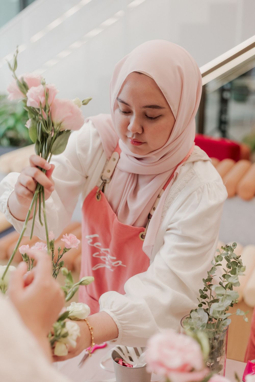 Participant carefully arranging pink flowers during a floral workshop session.