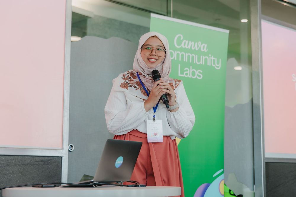 Presenter speaking at a Canva Community Labs event with green signage in the background.