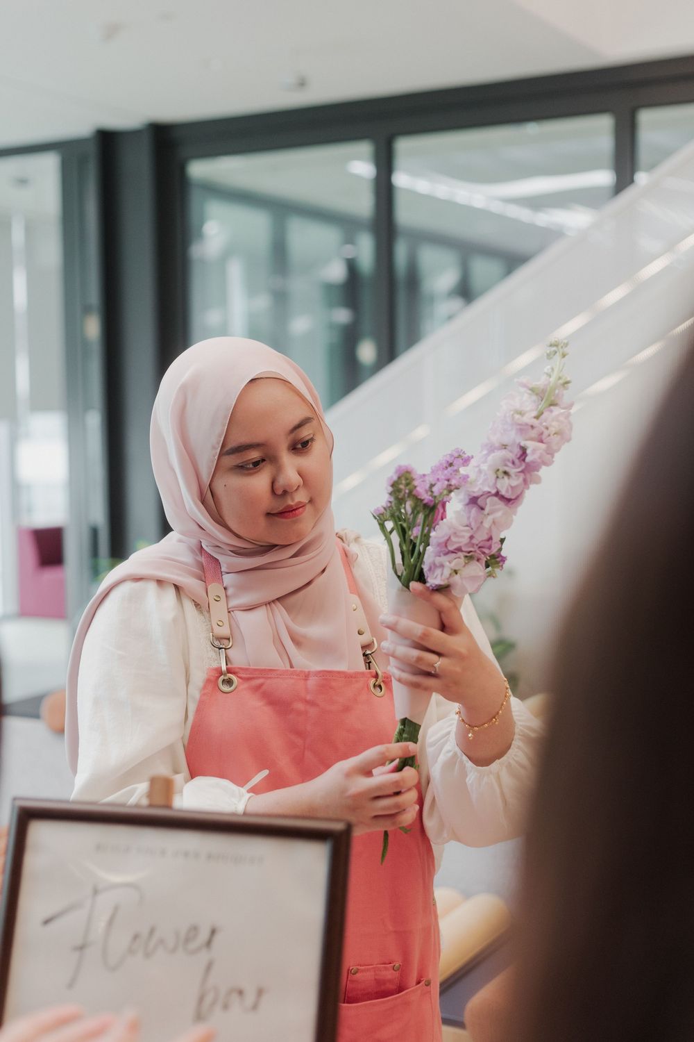 Workshop participant in pink attire arranging floral stems during a flower arranging session.