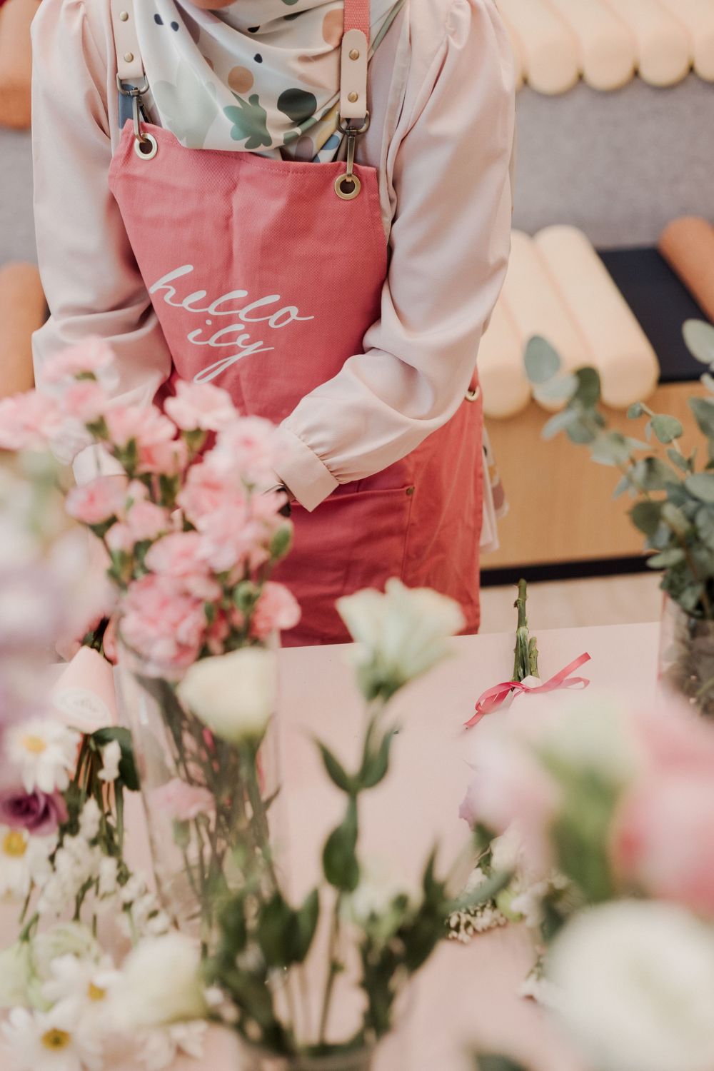 Person wearing a pink apron arranging delicate flowers at a floral workshop.