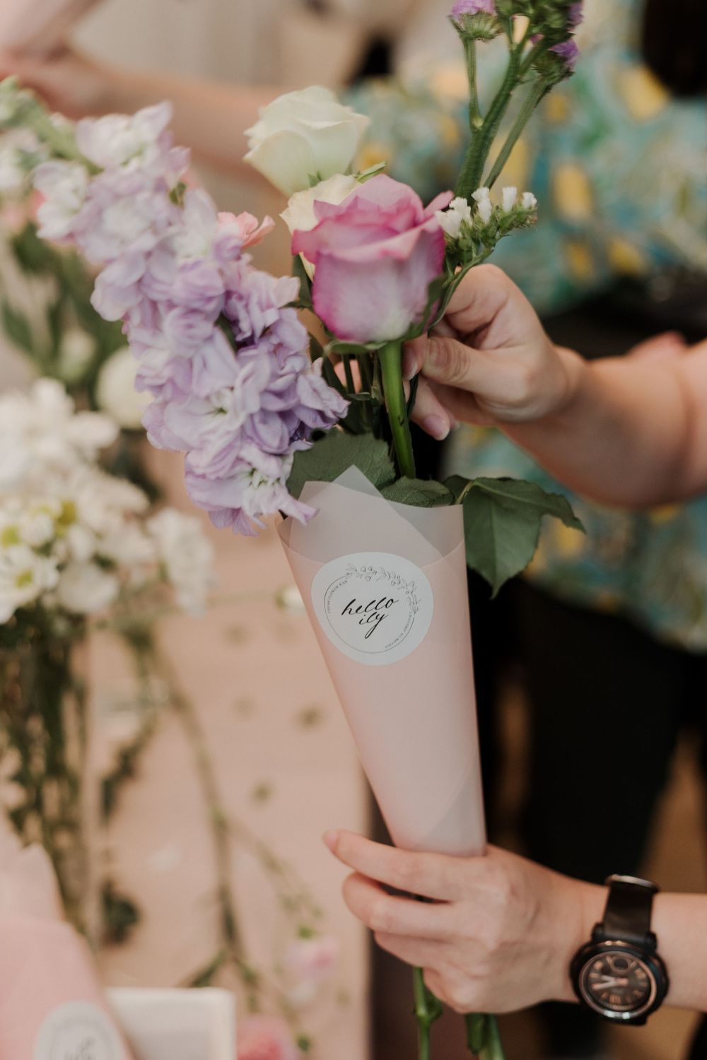 Fresh pink and purple flowers being arranged in a white branded vase.