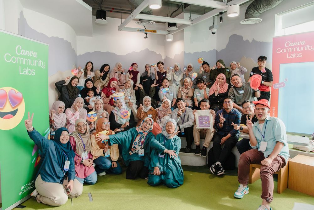 Large group photo of attendees at a Canva community event with colorful banners.