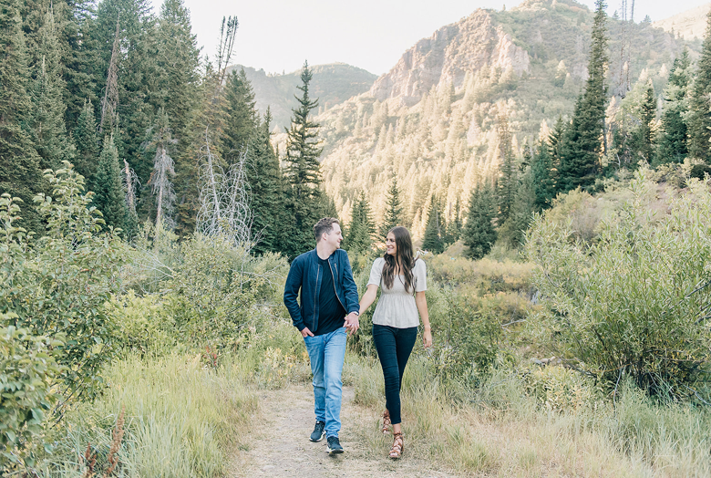 Couple hiking together on mountain trail surrounded by evergreen forest.