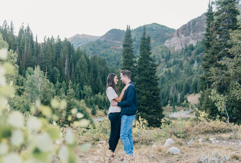 Romantic couple embracing on mountain trail with evergreen forest vista.