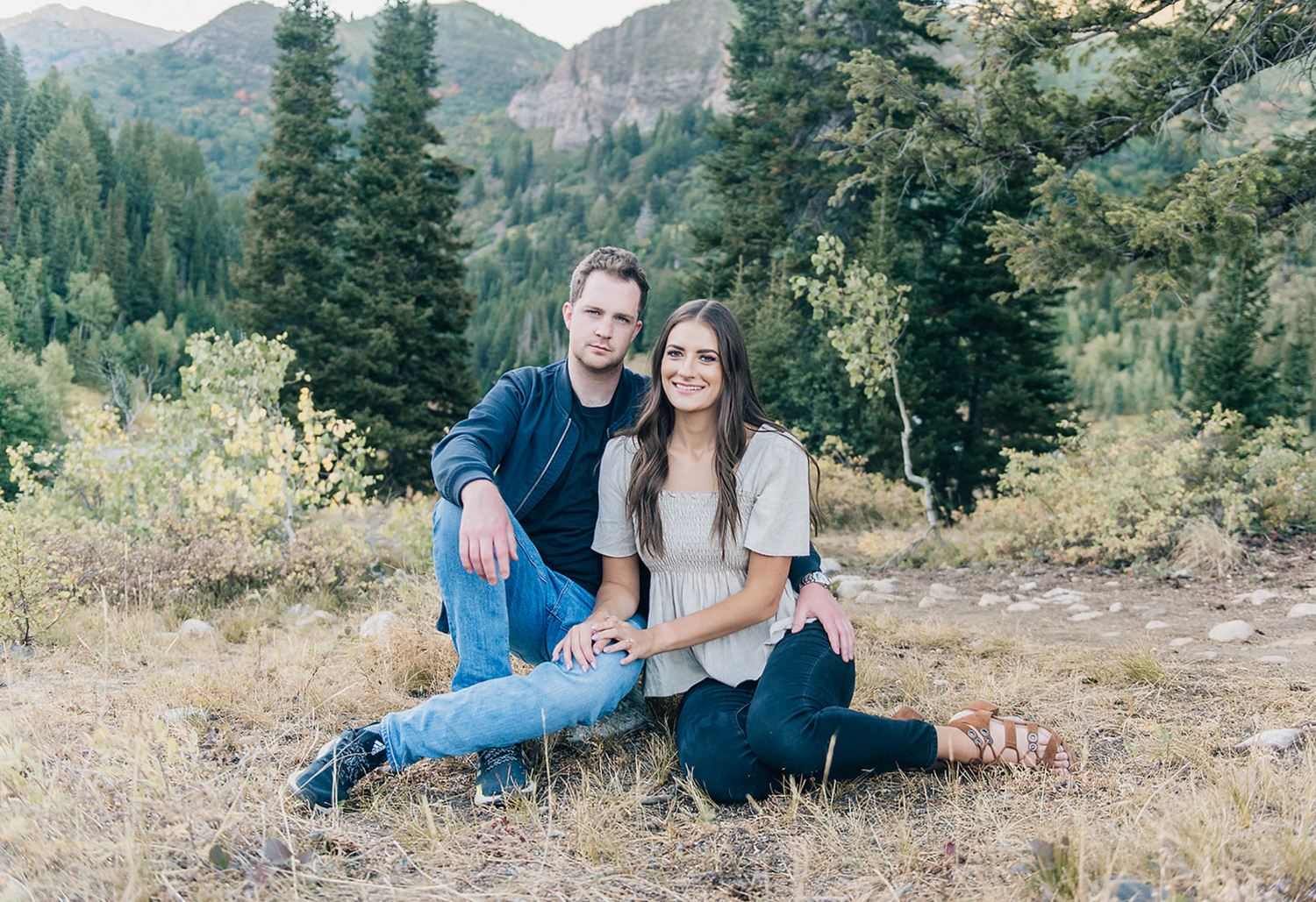 Couple sitting together on mountain trail with forest backdrop.