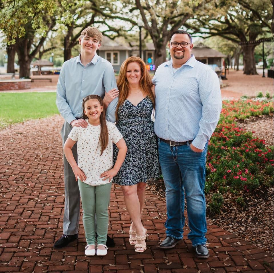 Family poses together on brick pathway surrounded by autumn landscaping.