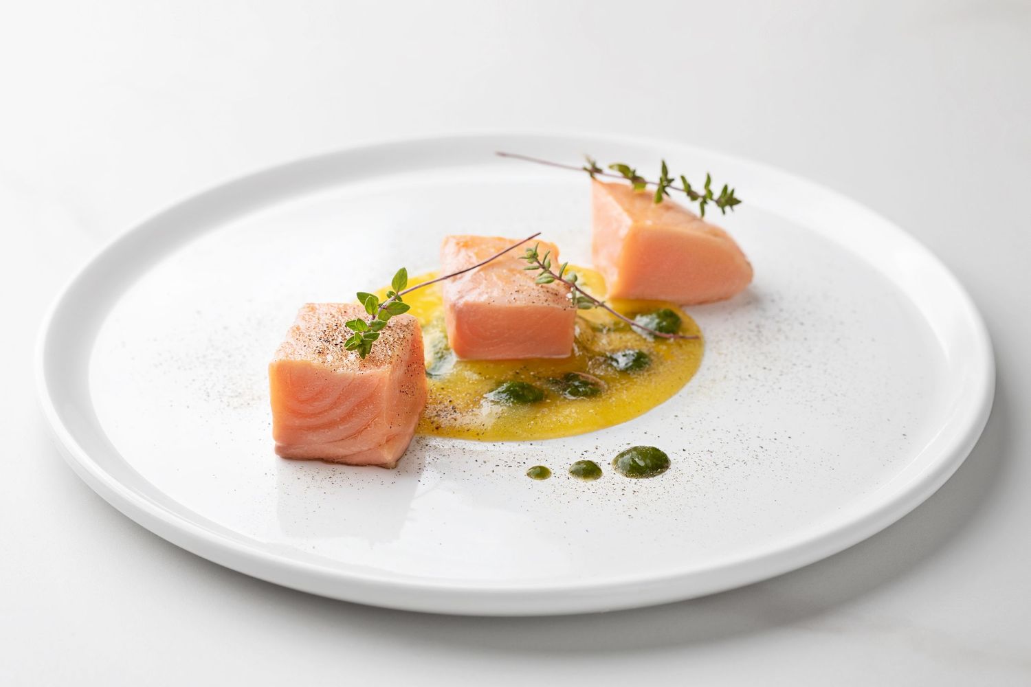 Elegant plated salmon dish with herb garnish and saffron sauce on a white plate, fine dining presentation.