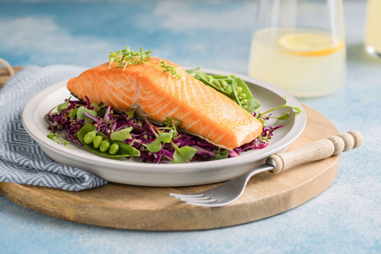 Grilled salmon fillet served on red cabbage salad with edamame and microgreens on a white plate.