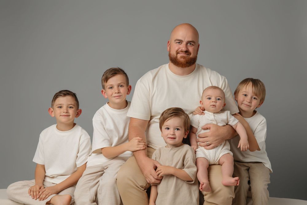Family portrait of a group in coordinated beige and white outfits against a neutral gray background.
