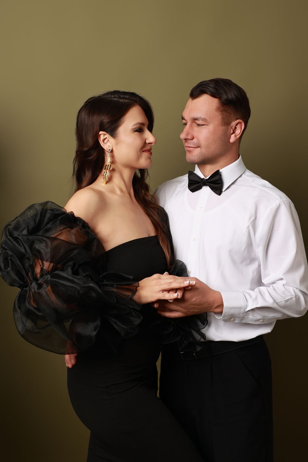 A couple in formal attire performs a romantic dance sequence in a studio setting against a dark background.